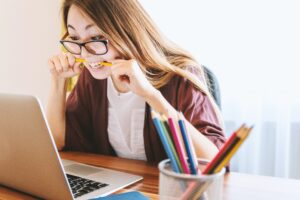 Student bites pencil while nervously studying on her computer.