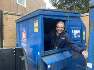 John stands inside a large dumpster