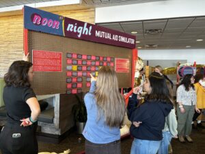 Attendees are interacting with the Noon at Night Mutual Aid Simulator, the game station portion of a carnival event focused on the climate crisis.