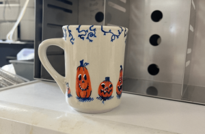 A painted mug with blue vines along the rim. There are happy jack-o-lanterns painted along the side of the white mug.