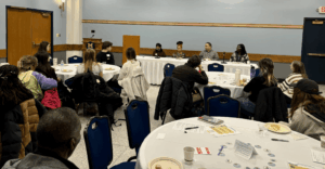 Photo of the "Climate Justice & Careers" event, showcasing the audience members seated at round tables. They all face the front of the room, where the moderator and panelists sit.