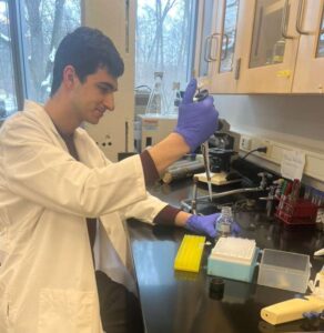 Photo of student researcher Alex Hamze holding a pipette in his right hand and a small glass bottle in his left.