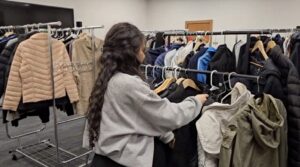 A student volunteer hangs jackets up on a clothing rack.
