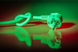 A white power cable tied in a knot lies on a reflective surface. It is illuminated by green and red lighting.