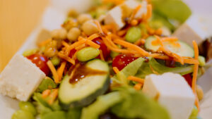 A close-up photo of salad from the dining halls. It has carrots, cucumbers, edamame, tofu, chickpeas, and tomatoes.