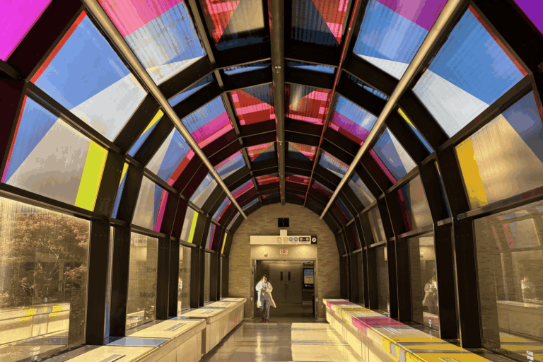 A medical professional walks in a brightly-lit skywalk in the hospital. The bridge is entriely surrounded by stained glass windows.