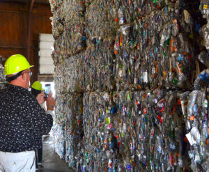 A person takes a photo of a wall of waste bales stacked on each other. Each bale is a rectangular prism of compressed trash.
