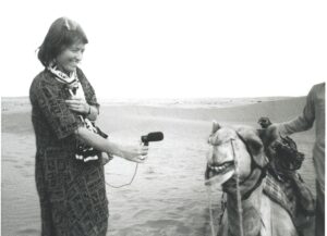 A photo of Hildegaard Westerkaamp smiling as she records a camel in the desert.